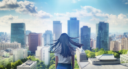 日本の街・都市・朝日を受けたオフィスビル群を前に佇み風を受けて髪をなびかせる会社員の女性の出勤　ビジネス・はじまり・決意・目標・挑戦のイメージ