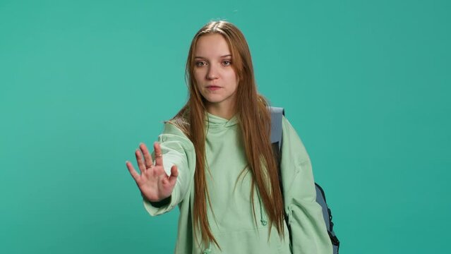 Assertive young woman doing stop hand gesture and talking. Annoyed girl doing firm halt sign gesturing, wishing to end concept, isolated over blue studio background, camera A