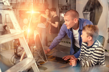 Fototapeta premium Interested young man with his tween son using computer to find solution to puzzle in escape room stylized as abandoned bunker. Toned image with visual effects