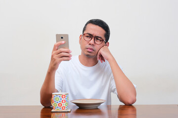 A man on dinning table looking to mobile phone with confused expression