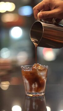 Pouring coffee into a glass of iced water on the table with blurred background