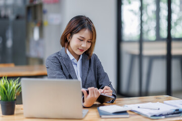 Asian Businesswoman Using laptop computer and working at office with calculator document on desk, doing planning analyzing the financial report, business plan investment, finance analysis concept.
