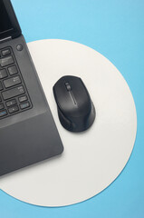 Laptop and pc mouse on blue background with white circle. Minimalism. Business concept