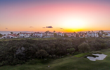 Aerial view of real estate development, luxury villas, single family homes in California near the Pacific Ocean over a gulf course with dramatic colorful sunset