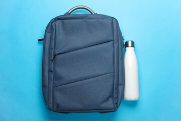Backpack with thermos bottle on a blue background. Top view