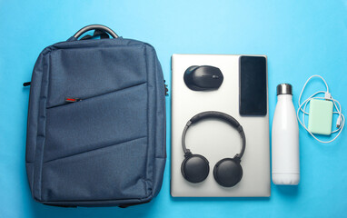 Laptop with Modern gadgets and accessories for work and study in Backpack on blue background. Top view. Flat lay