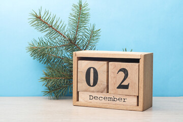 Wooden block calendar with date December 02 and pine tree on table and blue background