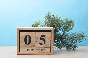 Wooden block calendar with date December 05 and pine tree on table and blue background