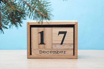 Wooden block calendar with date December 17 and pine tree on table and blue background