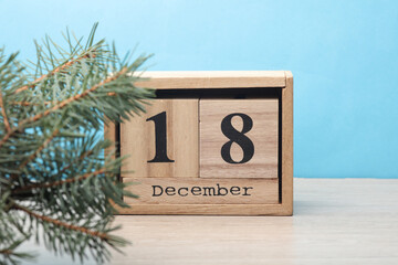 Wooden block calendar with date December 18 and pine tree on table and blue background