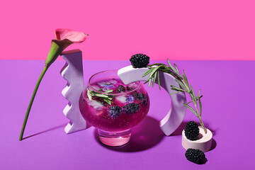 Glass of tasty blackberry cocktail with calla lily on color background