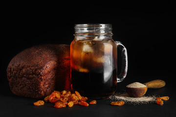 Mason jar of tasty kvass, yeast, bread and raisins on black background
