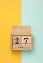 Wooden block calendar with date March 27 on blue yellow backround. Top view. Flat lay