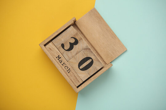 Wooden block calendar with date March 30 on blue yellow backround. Top view. Flat lay