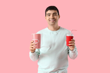 Happy young man with popcorn and soda on pink background