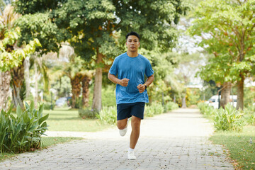 A man jogging on a paved path surrounded by greenery on a bright day with trees in the background