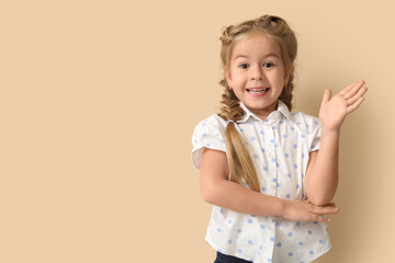 Happy little schoolgirl raising hand to ask question on beige background