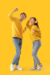 Young couple in headphones dancing on yellow background