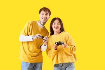Young couple playing video game on yellow background
