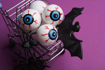 Minimalistic Halloween layout with eyeballs in a shopping cart, bats and spiders on purple...