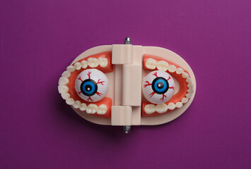 Minimalistic Halloween layout with eyeballs in jaw on purple background