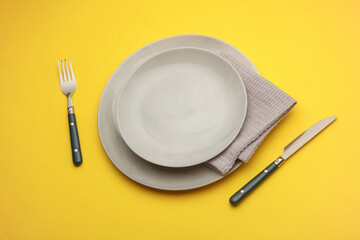 Plates, cutlery with towel on yellow background. Table setting. Top view