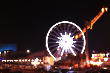 Glowing Ferris wheel in city at night, blurred view
