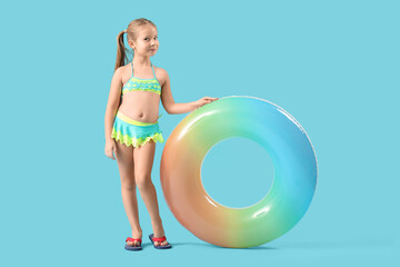Cute little girl in swimsuit with inflatable ring on blue background