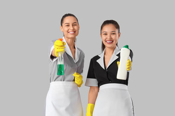 Young chambermaids with cleaning supplies on light background