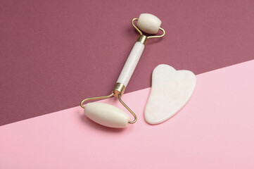 Massage roller and gua sha scraper for anti-aging facial massage on pink burgundy background