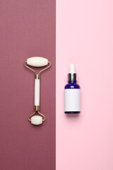 Massage roller and serum bottle for anti-aging facial massage on a pink burgundy background