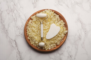 Jade facial roller and gua sha scraper on sea salt. Beauty concept