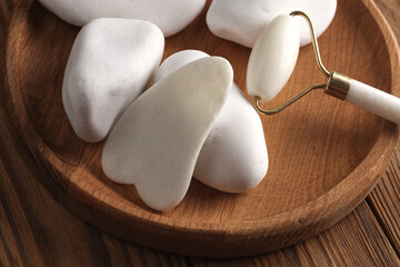 Jade facial roller and gua sha scraper, pebbles on wooden background. Beauty concept.