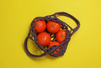 String bag with tangerines on a yellow background. Top view
