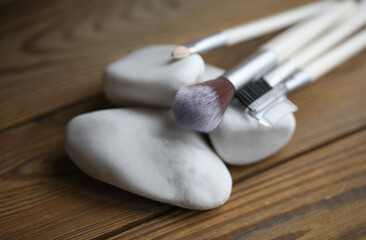 Set of makeup brushes with pebbles on a wooden background