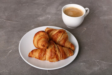 Plate with tasty croissants and cup of coffee on grey background