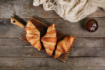 Board with tasty croissants and bowl of jam on wooden table