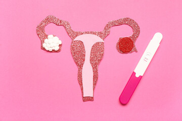 Paper uterus with pregnancy test on pink background