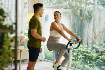 A man and woman smiling at each other during a workout session with the woman on a stationary bike