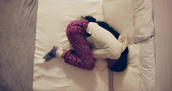 Woman, sad and stomach pain in bed with PMS, cramps and crying in high angle at home. Person or above with stress, frustrated or agony and lying with pillow for endometriosis, uterus and health risk
