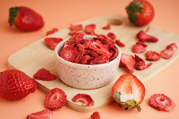 Bowl with tasty freeze-dried strawberries on orange background