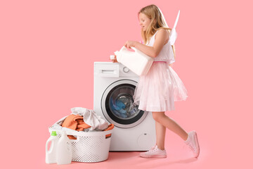 Girl in fairy costume with bottle of laundry detergent near washing machine and basket with dirty...