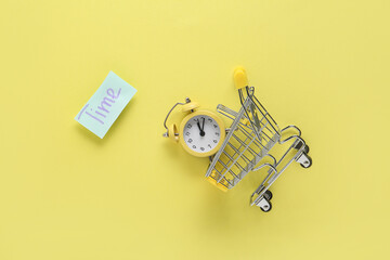 Paper with word TIME, tiny shopping cart and alarm clock on yellow background. Time management...