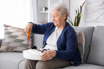 Senior woman with screwdriver and robot vacuum cleaner at home