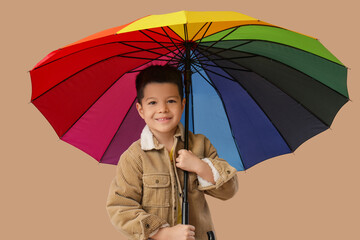 Cute little Asian boy with umbrella on beige background
