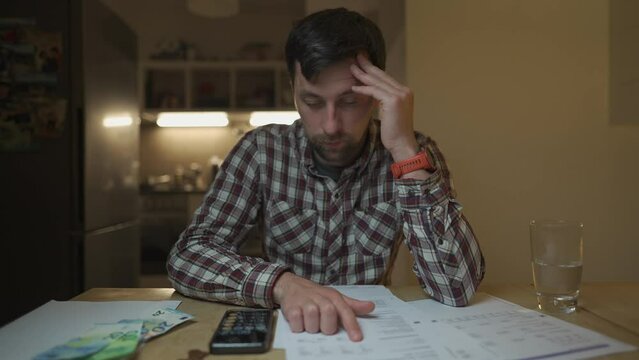 Financial problems. Sad man trying to find solution to taxes and debts at home in kitchen. Brainstorming ways of solving money troubles. Stressed male calculates costs, try to keep money in savings. 