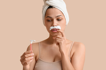 Beautiful young thoughtful woman with razor and shaving foam on beige background. Depilation concept