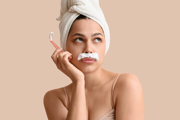 Beautiful young thoughtful woman with razor and shaving foam on beige background. Depilation concept