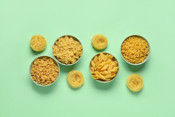 Bowls with different tasty uncooked pasta on green background