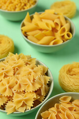 Bowls with different tasty uncooked pasta on green background, closeup